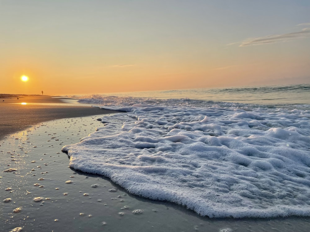 the sun is setting over the ocean with waves coming in