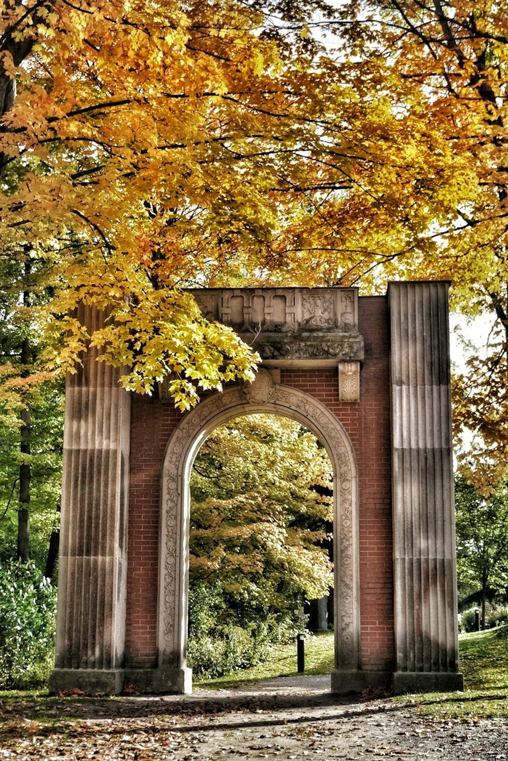 a stone arch in a park surrounded by trees