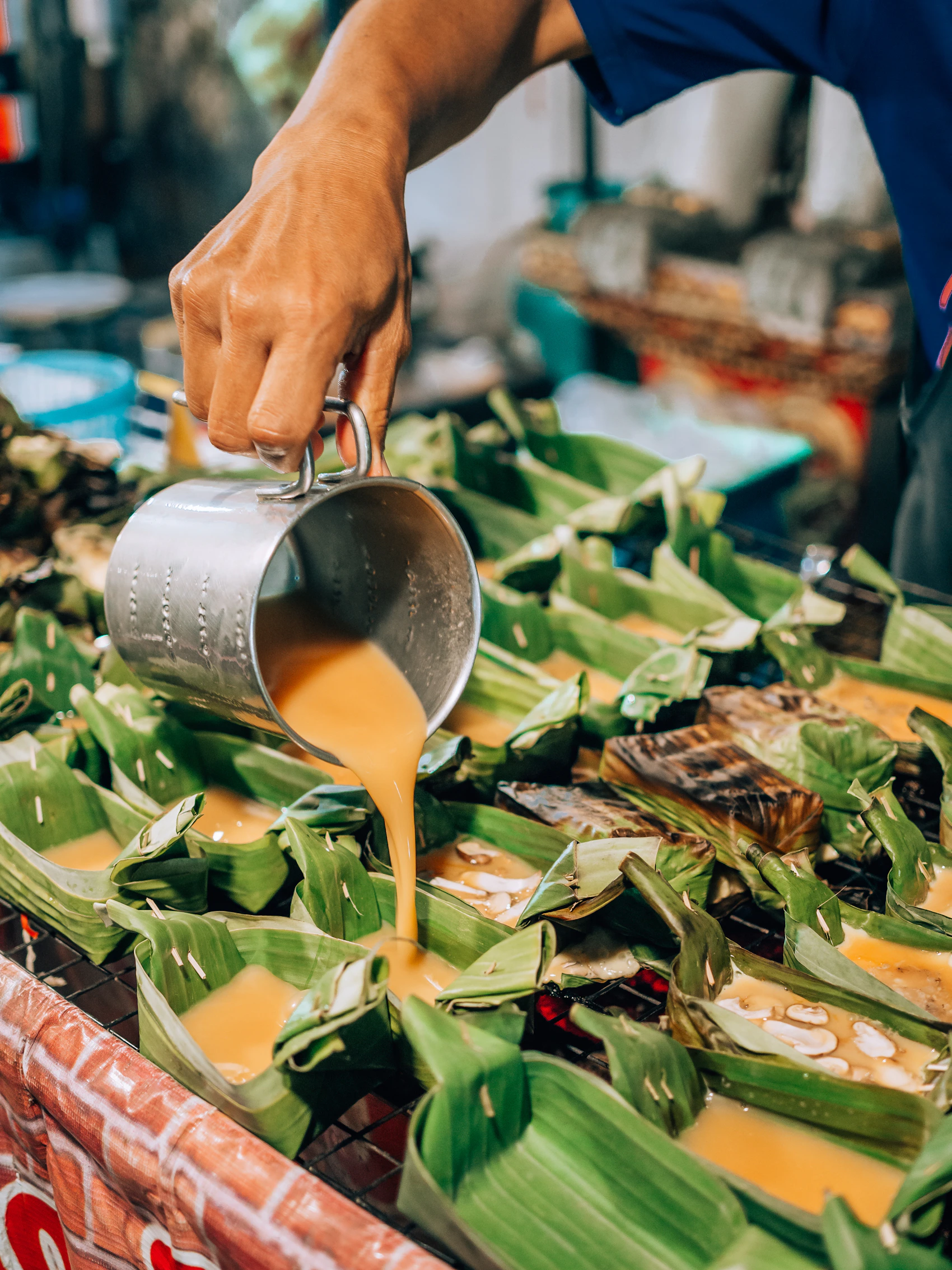 A Chiang Mai market cook pouring coconut mixture into banana-leaf parcels