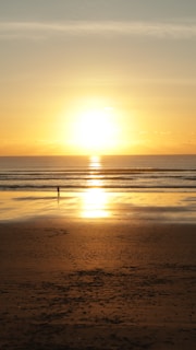 A serene beach scene with a lone traveler walking along the shore at golden hour.