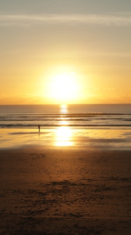 A serene beach scene with a lone traveler walking along the shore at golden hour.