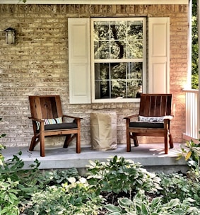 two wooden chairs sitting on a porch next to a window