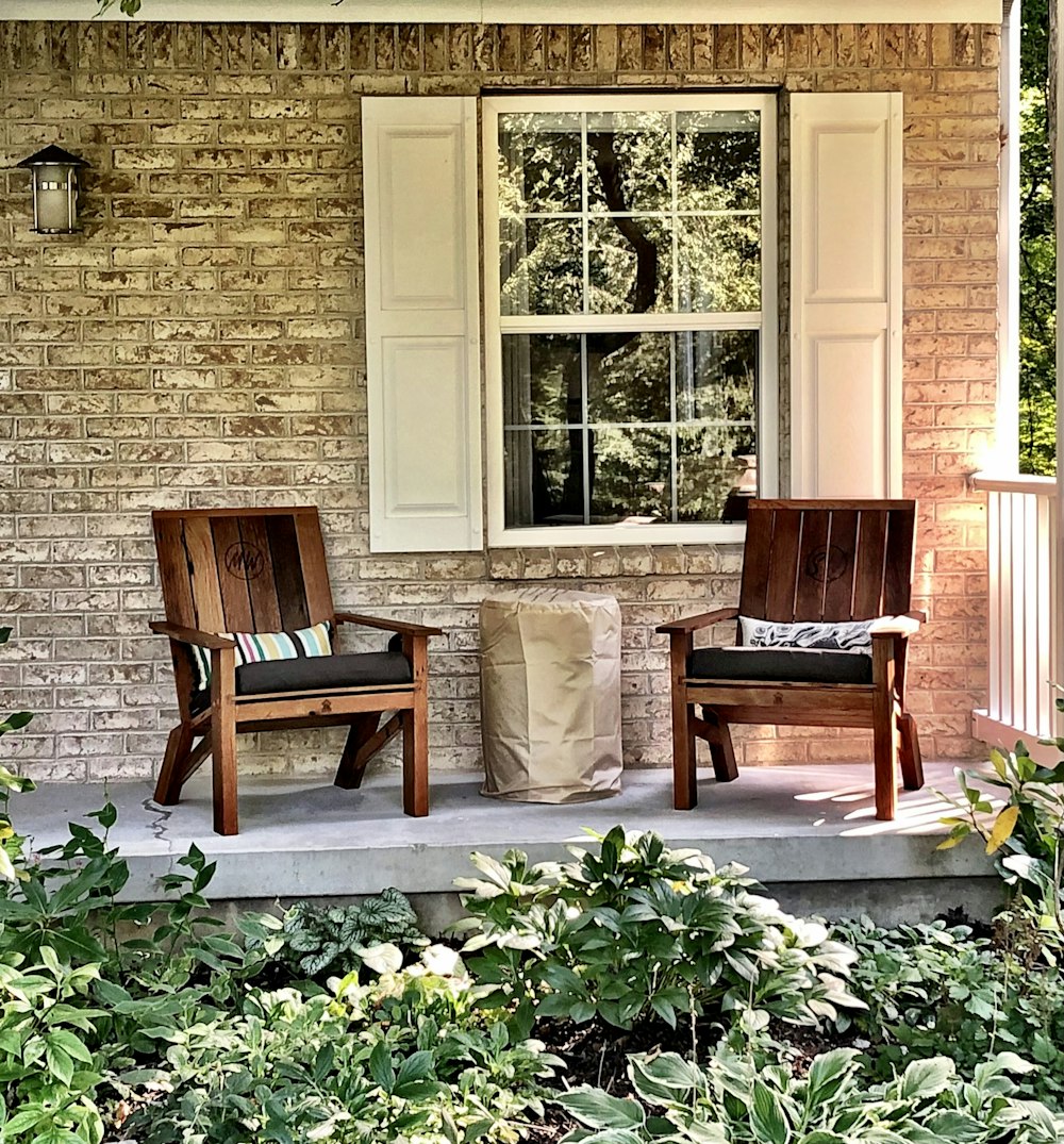 two wooden chairs sitting on a porch next to a window