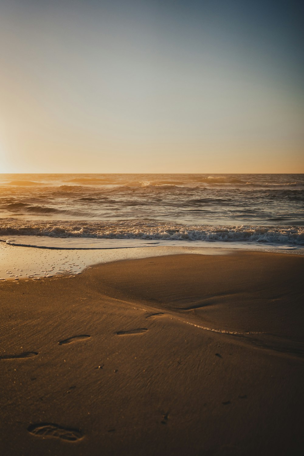 the sun is setting over the ocean with footprints in the sand