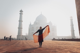 a woman holding a scarf in front of The Taj-Mahal at sunrise.