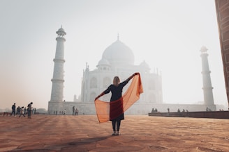 a woman holding a scarf in front of The Taj-Mahal at sunrise.