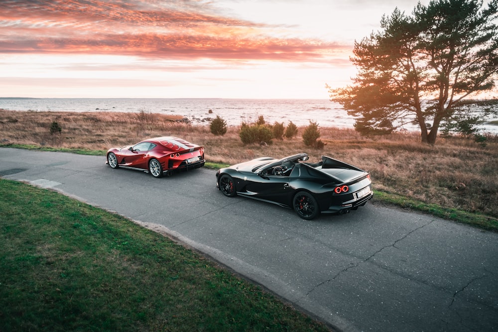 two sports cars driving down a road next to the ocean