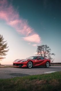A classic red sports car parked on a scenic mountain road at sunset.