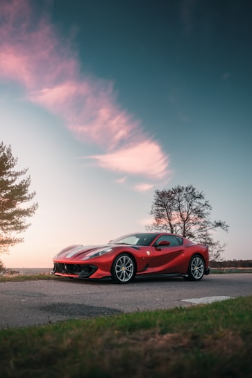 A classic red sports car parked on a scenic mountain road at sunset.