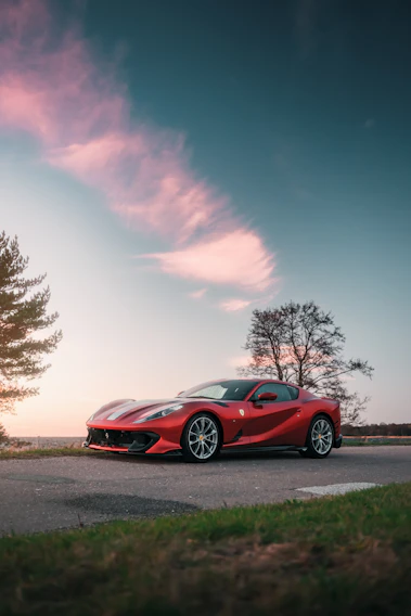 A sleek red hatchback parked on a scenic mountain road during sunset.