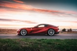 A sleek red sports car speeding along a coastal highway at sunset.