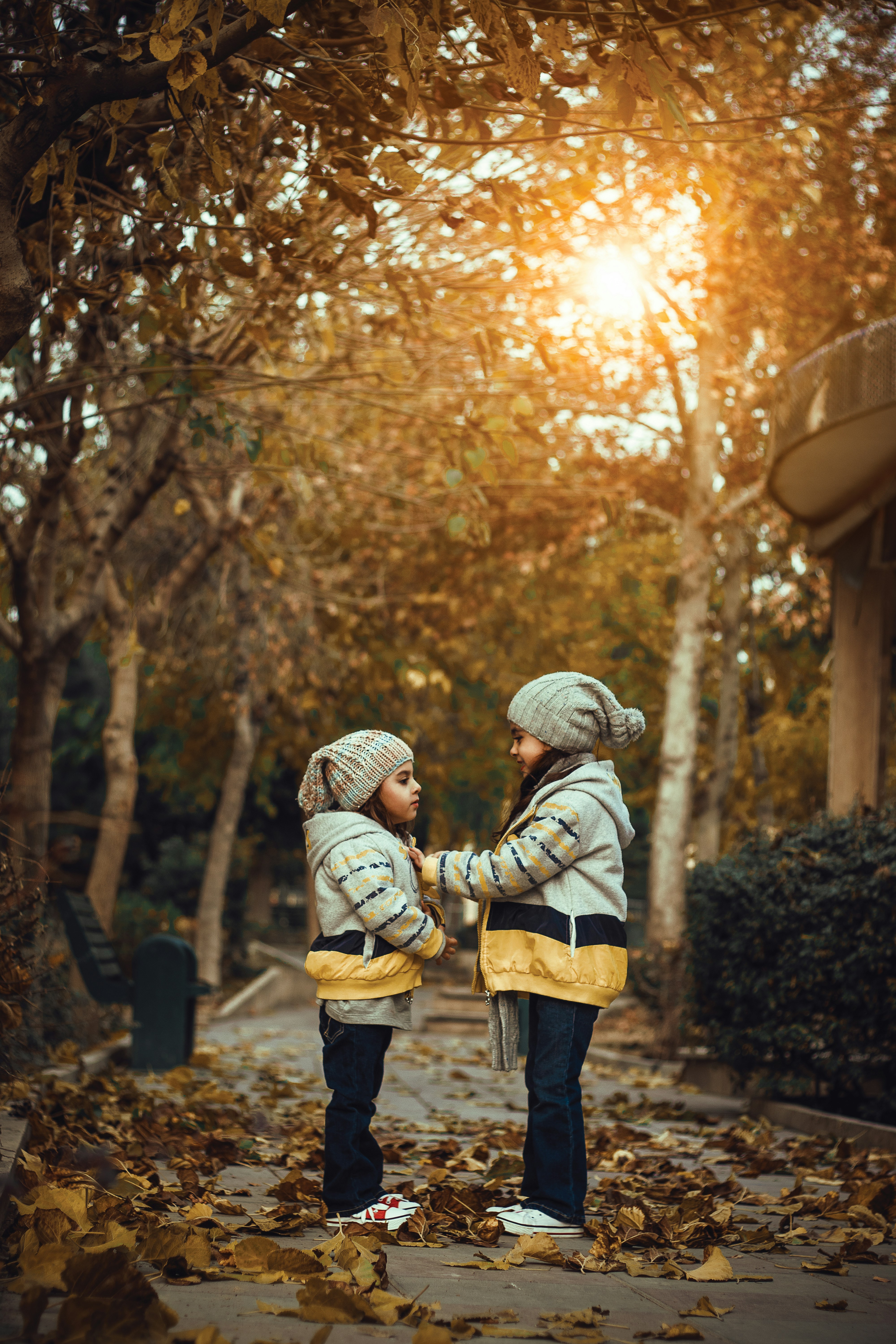 duas meninas de pé em uma calçada coberta de folhas