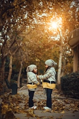 two little girls standing on a leaf covered sidewalk