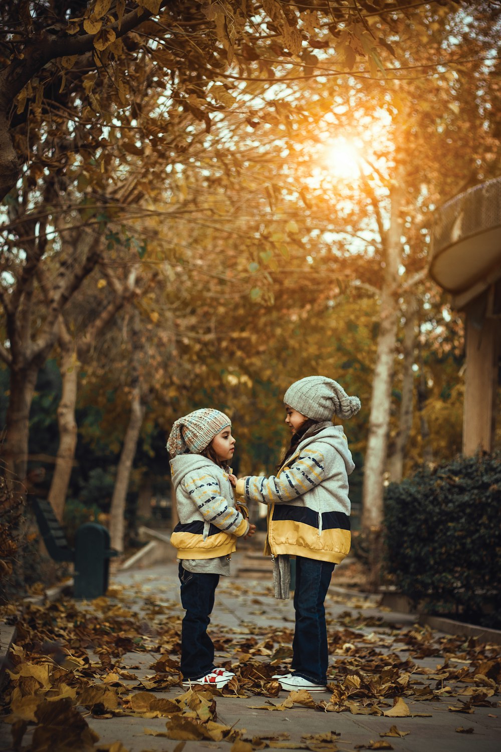 two little girls standing on a leaf covered sidewalk