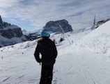 An adult skier adjusting their helmet strap against a backdrop of snowy mountains.