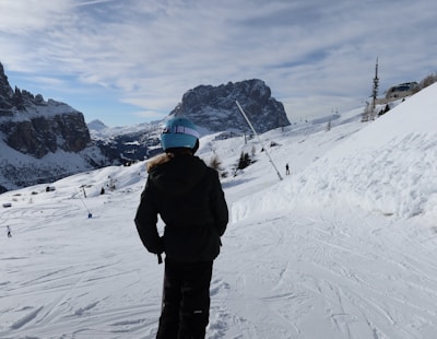 An adult skier adjusting their helmet strap against a backdrop of snowy mountains.