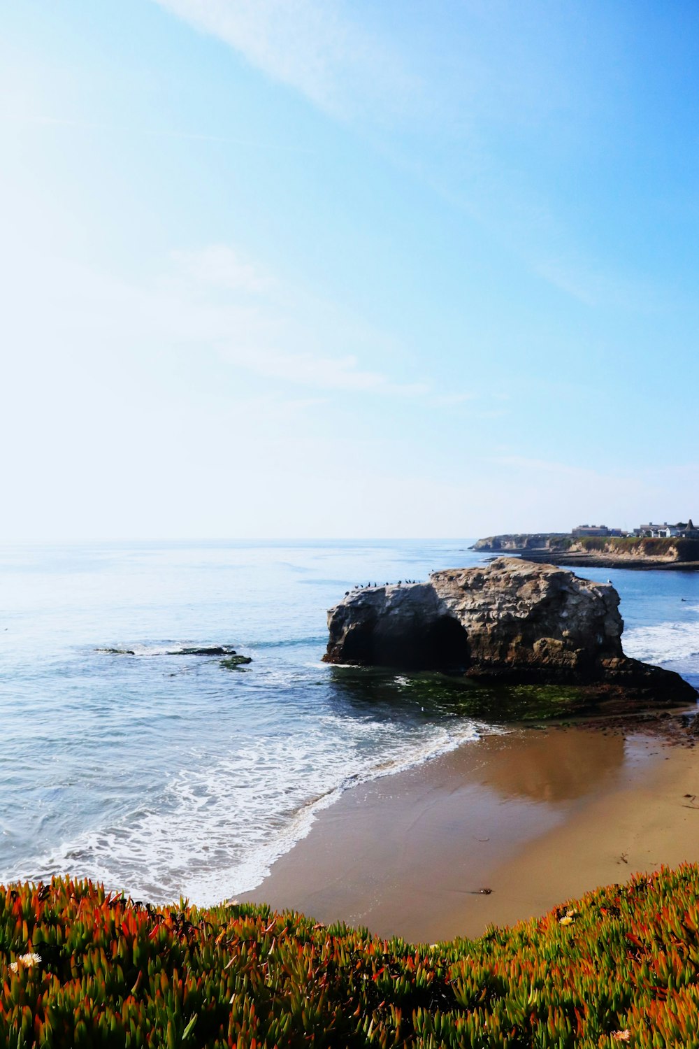 a view of a beach with a rock outcropping in the water