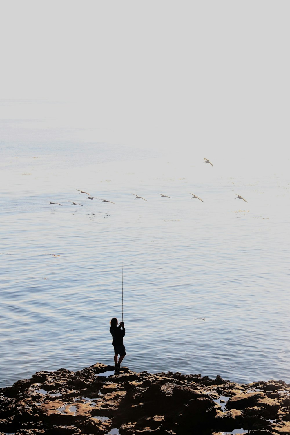 a person standing on a rock with a fishing rod