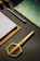 A set of neatly arranged stationery items is on a dark textured surface. There is a gold pair of scissors with a modern design, a stack of paper on a clipboard, a pen, and a decorative notebook with a green and white pattern.