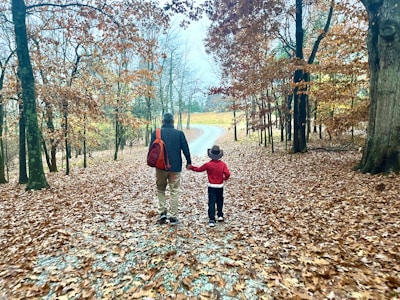 A candid shot of a father and daughter walking together along a tree-lined path in autumn.