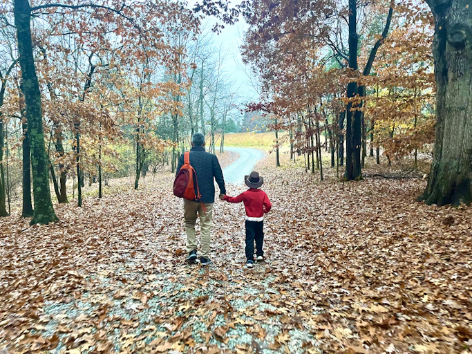 A candid shot of a father and daughter walking together along a tree-lined path in autumn.