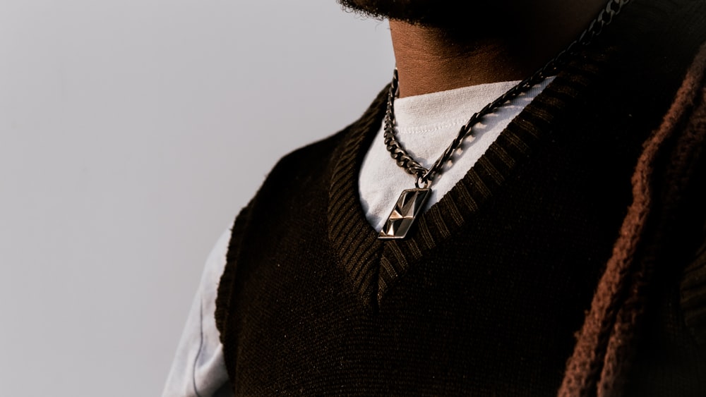 a man wearing a sweater vest and a necklace