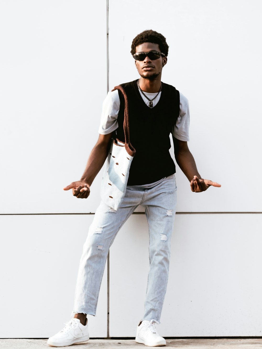 a man in a vest and sunglasses leaning against a wall