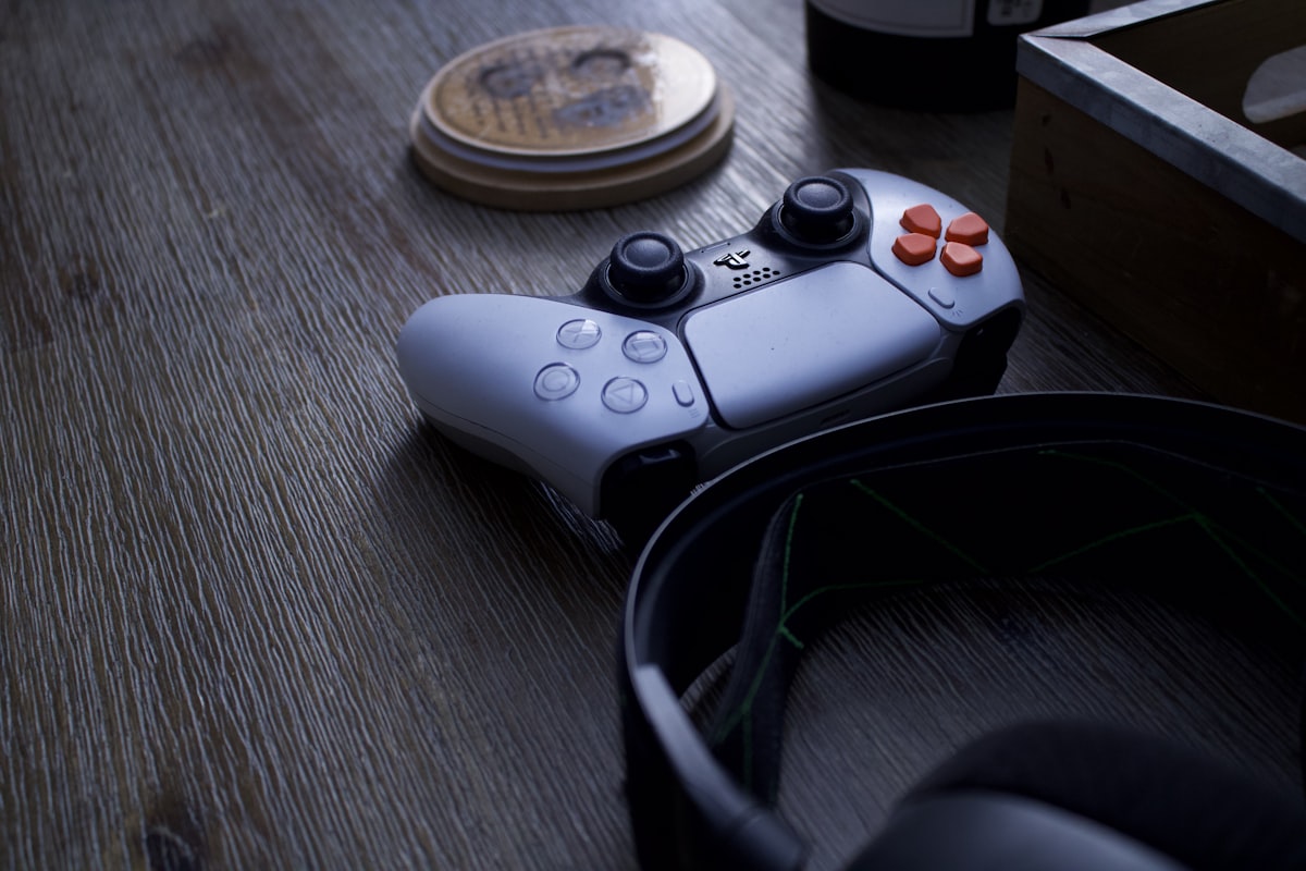 A video game controller sitting on a wooden table next to gaming headphones