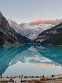 a group of people standing around a lake with mountains in the background