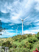 Aerial shot of wind turbines aligned along a green hillside with blue skies