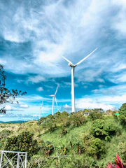 Wind turbines turning gently on a green hillside with a bright blue sky