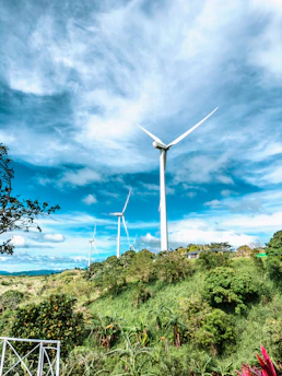 Wind turbines turning gently on a green hillside with a bright blue sky