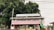 A structure with a corrugated metal roof is situated outdoors, featuring a prominent sign that reads 'Layanan Wifi Gratis' in large letters. Additional text in smaller letters indicates the involvement of a governmental department in the local area, Dinas Komunikasi Informatika dan Statistik Kabupaten Ponorogo. The structure is surrounded by trees and other outdoor elements.