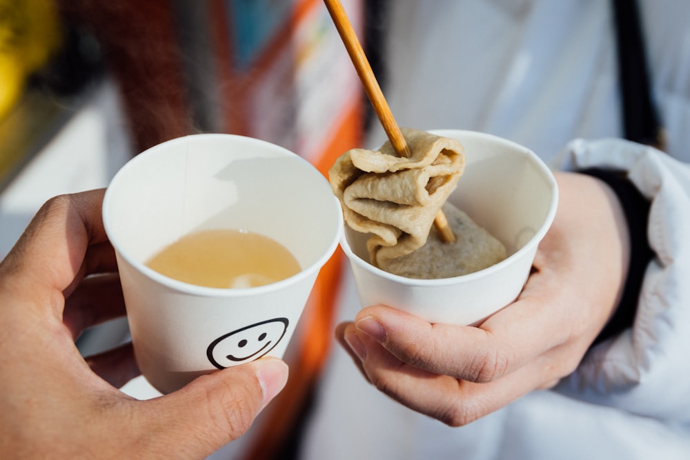 a person holding a cup of soup with chopsticks in it