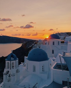 A serene sunset over the whitewashed buildings of Santorini with the Aegean Sea in the background.