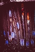 Intricate braids adorned with blue beads hanging down, with a sparkling, textured background. A hint of a person's face partially covered by the braids.