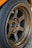 A close-up view of a metallic alloy wheel featuring a five-spoke design. The wheel is mounted on a car with a visible tire surrounding it. The surface of the wheel is slightly worn, indicating use, and branding logos are present on the spokes.
