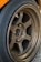 A close-up view of a metallic alloy wheel featuring a five-spoke design. The wheel is mounted on a car with a visible tire surrounding it. The surface of the wheel is slightly worn, indicating use, and branding logos are present on the spokes.