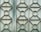 A metal gate featuring a geometric design with repeating patterns of circles and diamonds. The surface appears weathered and slightly rusty, with a faded bluish-green color.