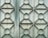A metal gate featuring a geometric design with repeating patterns of circles and diamonds. The surface appears weathered and slightly rusty, with a faded bluish-green color.