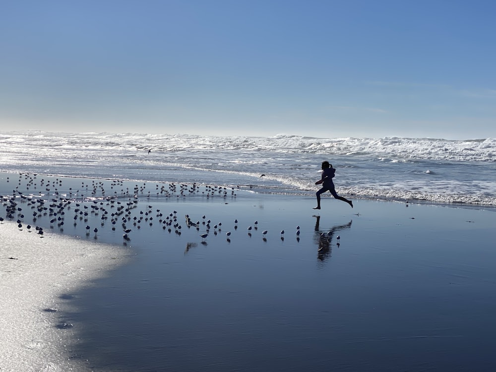 a person running on a beach with a flock of birds
