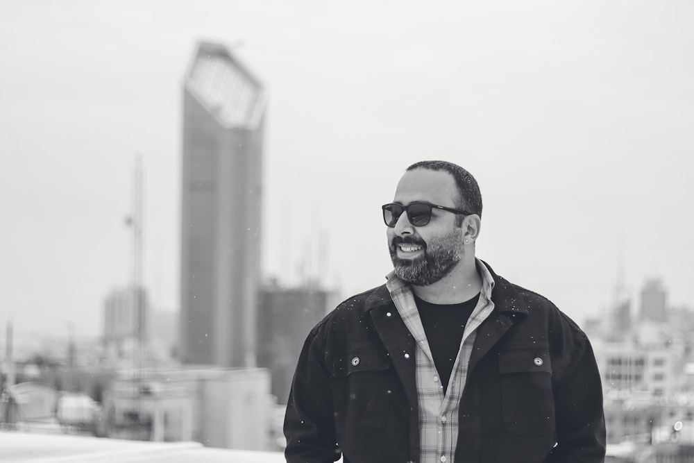 a man with a beard and sunglasses standing in front of a city skyline