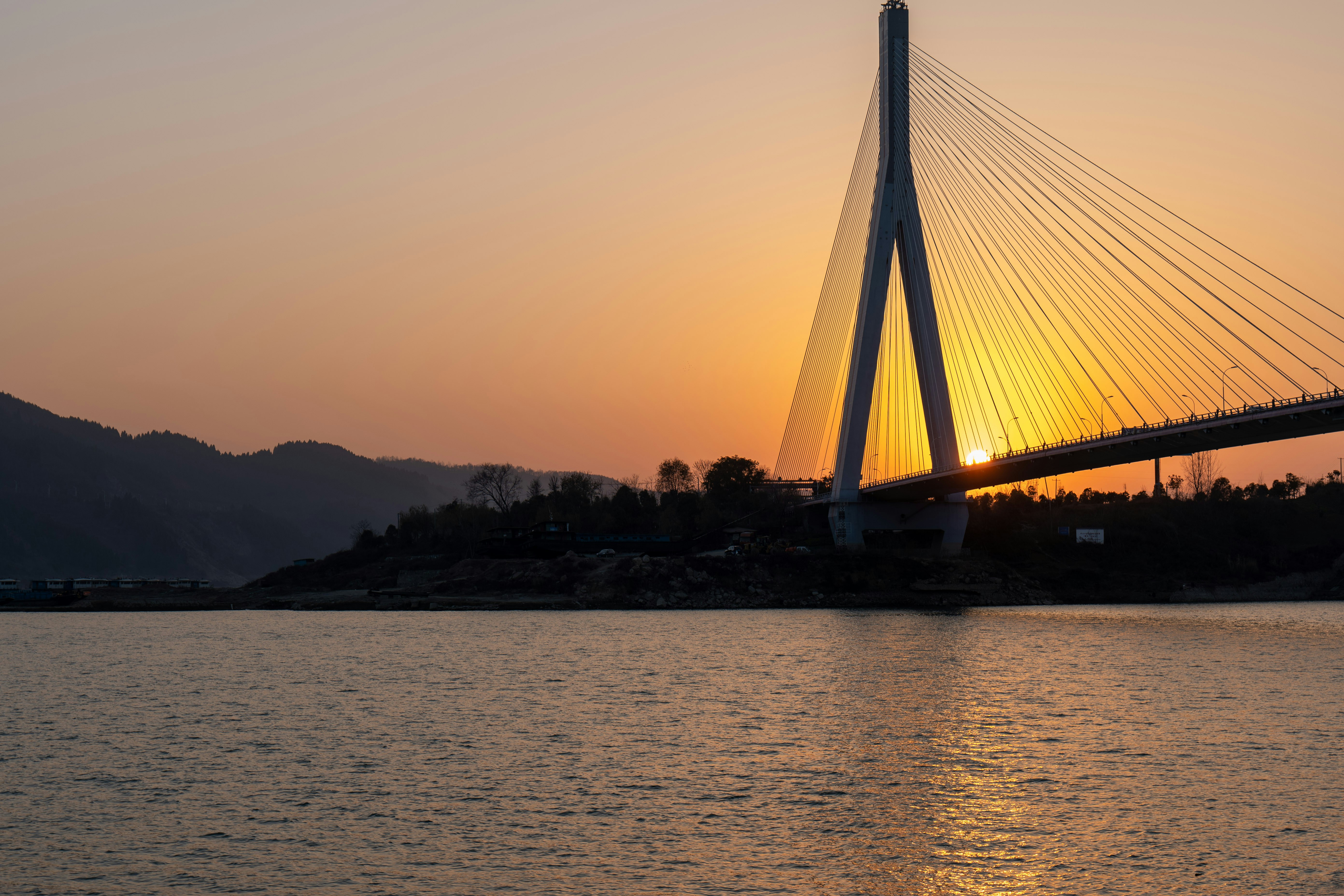 The sun is setting behind a bridge over a body of water