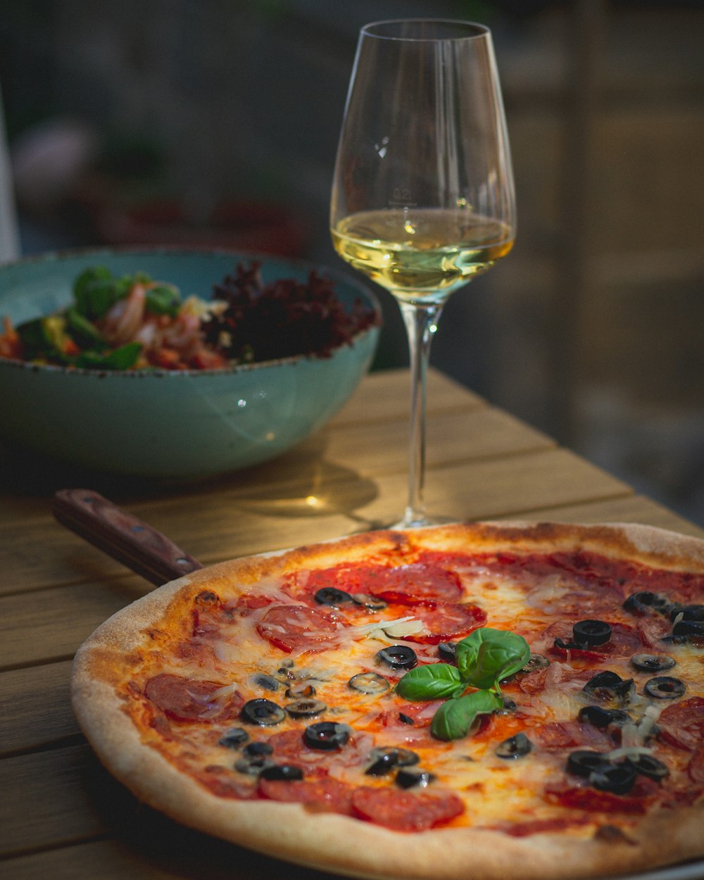 a pizza sitting on top of a wooden table next to a glass of wine
