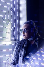 a woman wearing sunglasses and a scarf standing in front of a wall with lights