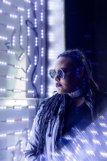 a woman wearing sunglasses and a scarf standing in front of a wall with lights