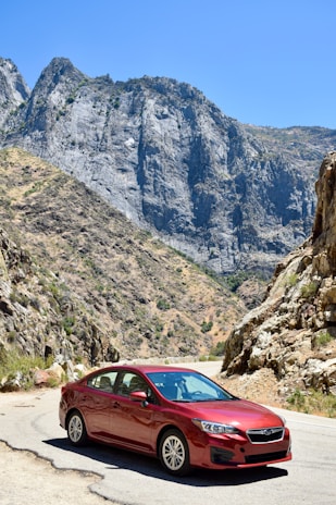 A shiny red sports car parked on a winding mountain road under a clear blue sky.