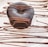 A rich, dark chocolate dessert with a smooth surface, elegantly drizzled with chocolate sauce. The dessert sits on a white plate with artistic, flowing lines of chocolate as decoration.