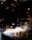 A taxi driving through a city street at night with steam rising from vents in the pavement. The scene is illuminated by the lights from surrounding tall buildings and reflections on the wet road surface.