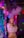 A person standing in a vibrant, colorful setting with neon lights and party decorations. The individual is holding a vaping device, exhaling a large cloud of vapor. The background is decorated with shiny, metallic streamers and balloons, creating a festive atmosphere.